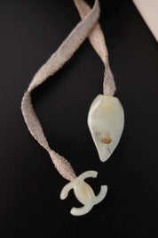 Small interlocking CHANEL CC logo charm at the end of the vintage textile ribbon necklace