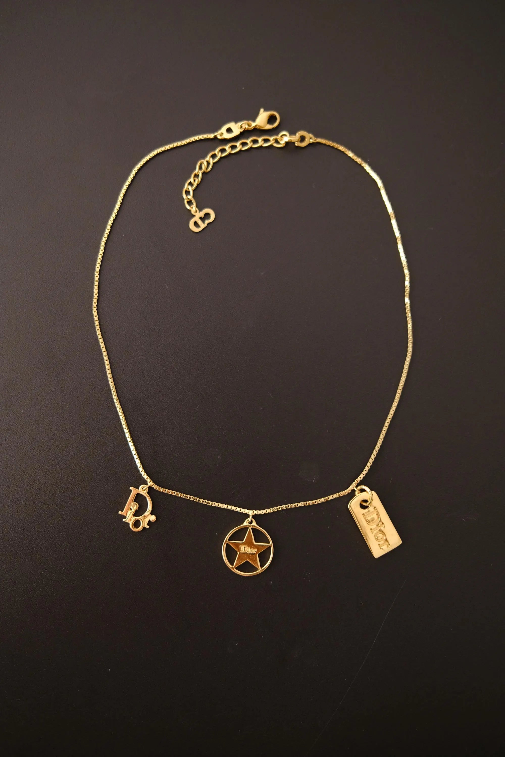 Full view of vintage Christian Dior gold tone chain necklace with three dangling signature Dior charms and adjustable extender