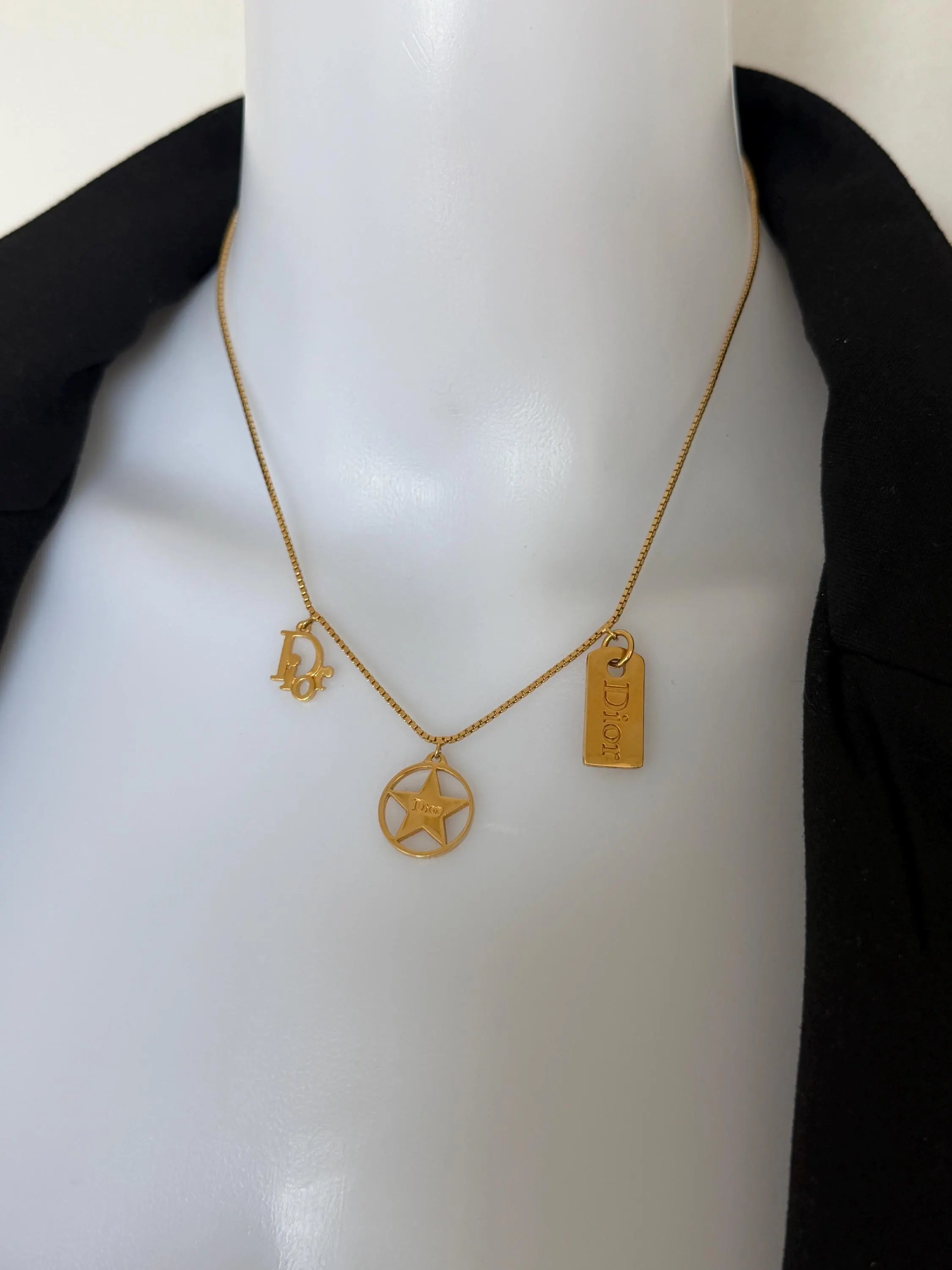 Close-up of three vintage Christian Dior gold charms featuring CD monogram, openwork star and rectangular Dior logo tag