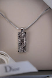 Close-up of textured repeating Dior monogram design on vintage rectangular pendant necklace