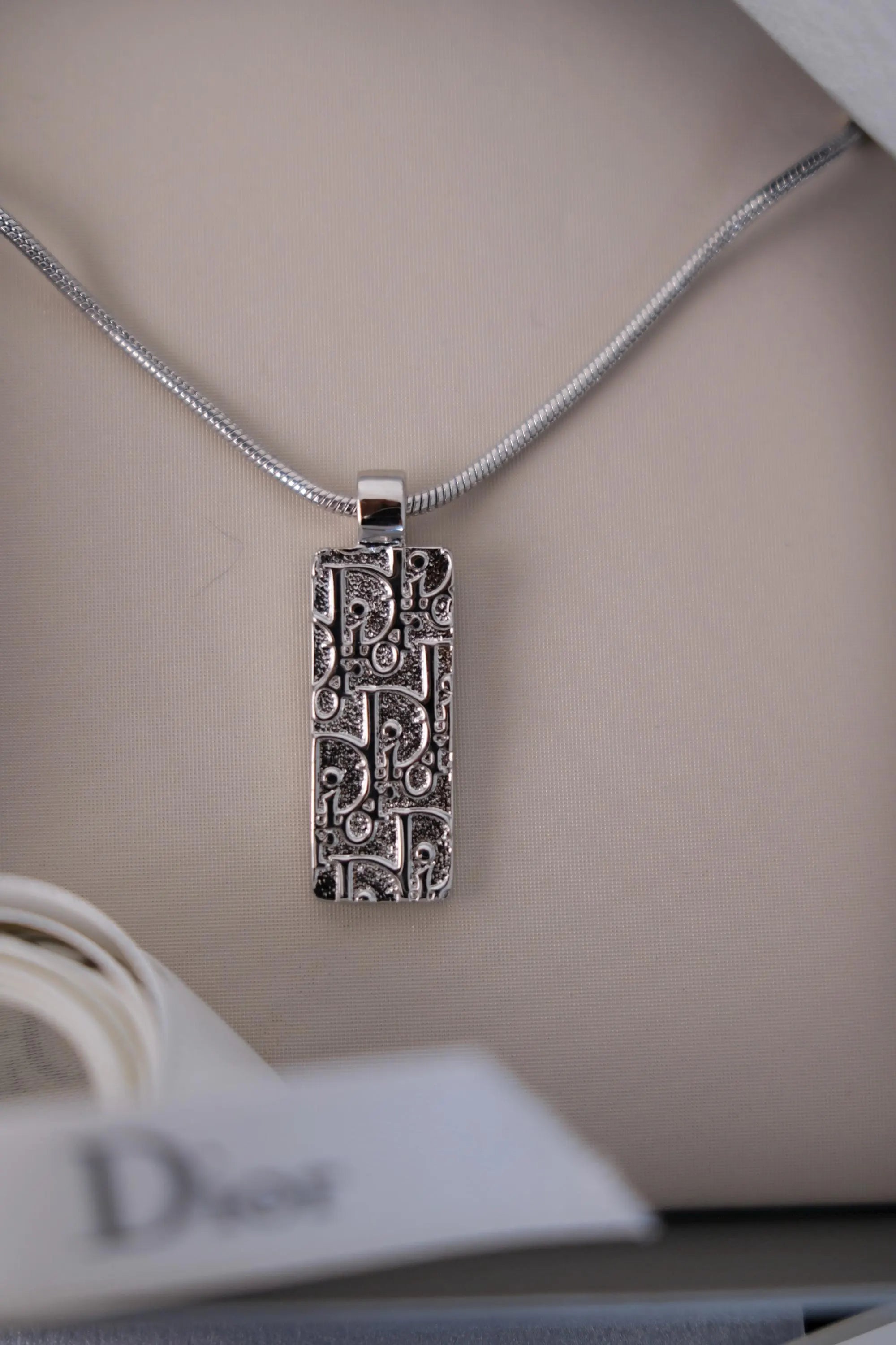 Close-up of textured repeating Dior monogram design on vintage rectangular pendant necklace