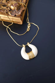 Vintage Givenchy ivory white horseshoe pendant necklace with Greek key gold tone accents and delicate chain on dark background