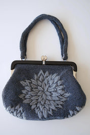 Front view of vintage Japanese glass beaded handbag with large dimensional silver-grey peony flower against blue-grey beaded background