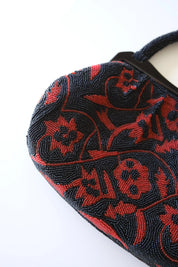 Close-up of intricate Japanese glass seed bead embroidery with deep red flowers and black scrolling vine patterns