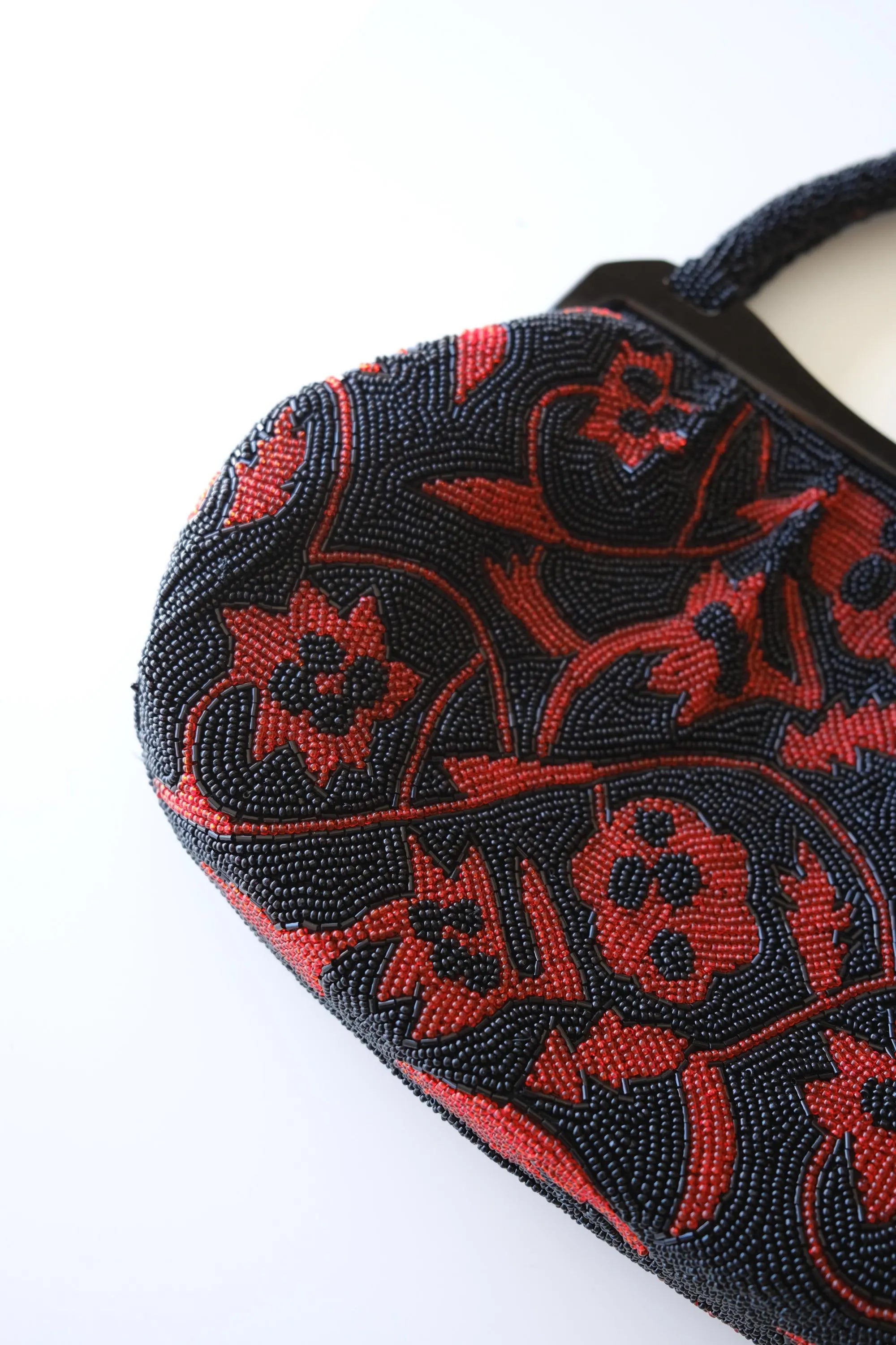 Close-up of intricate Japanese glass seed bead embroidery with deep red flowers and black scrolling vine patterns