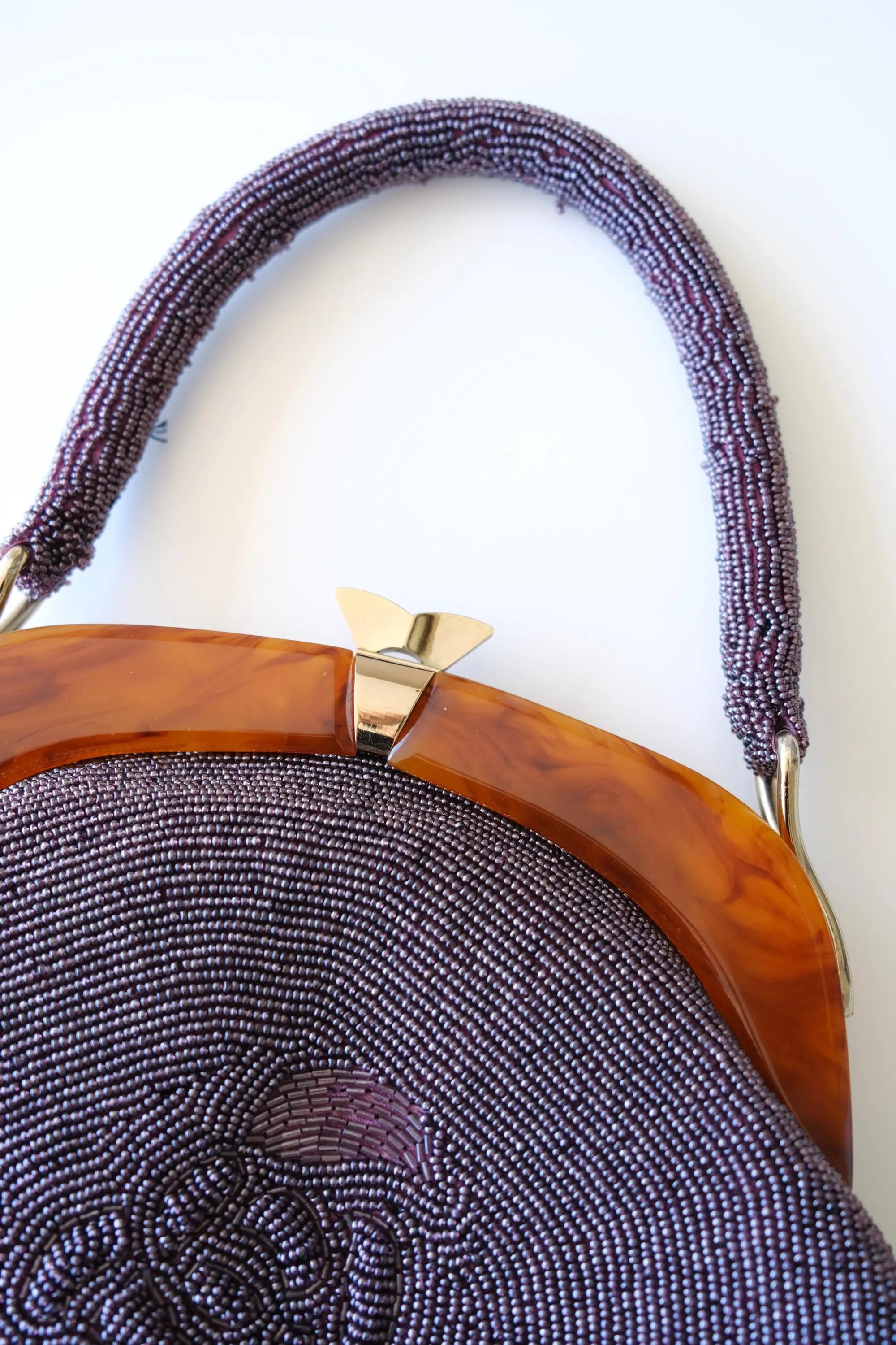 Close-up of decorative gold-tone clasp closure on amber-tone frame of vintage Japanese purple beaded handbag