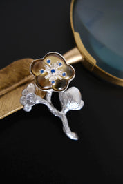 Full view of vintage KENZO floral branch brooch featuring silver tone leaves, champagne gold flower and blue crystals