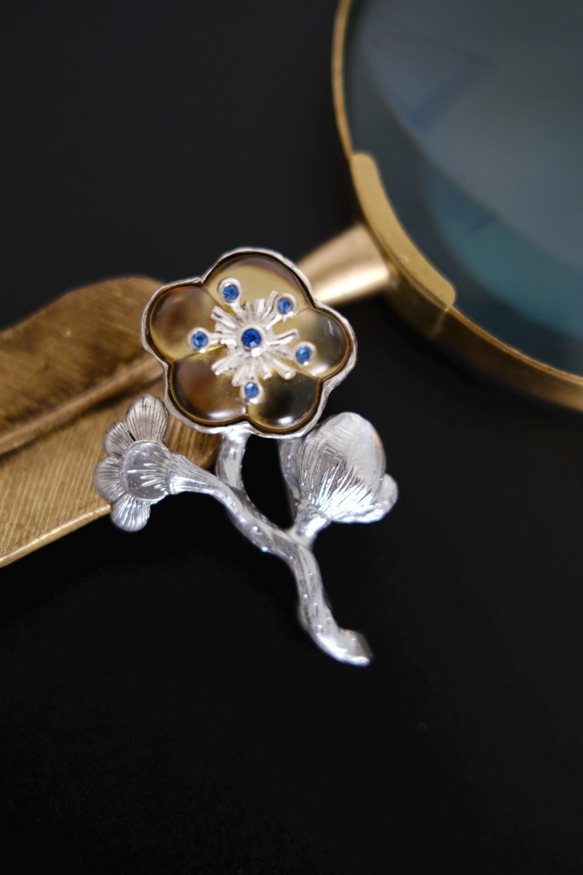 Full view of vintage KENZO floral branch brooch featuring silver tone leaves, champagne gold flower and blue crystals