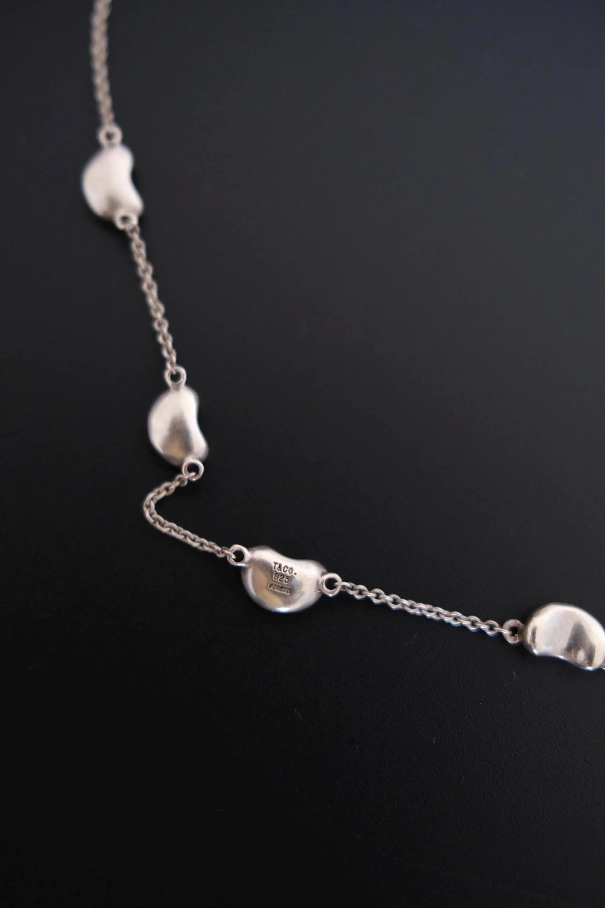 Close-up of TIFFANY & CO signature marking on vintage Elsa Peretti Five Bean silver necklace
