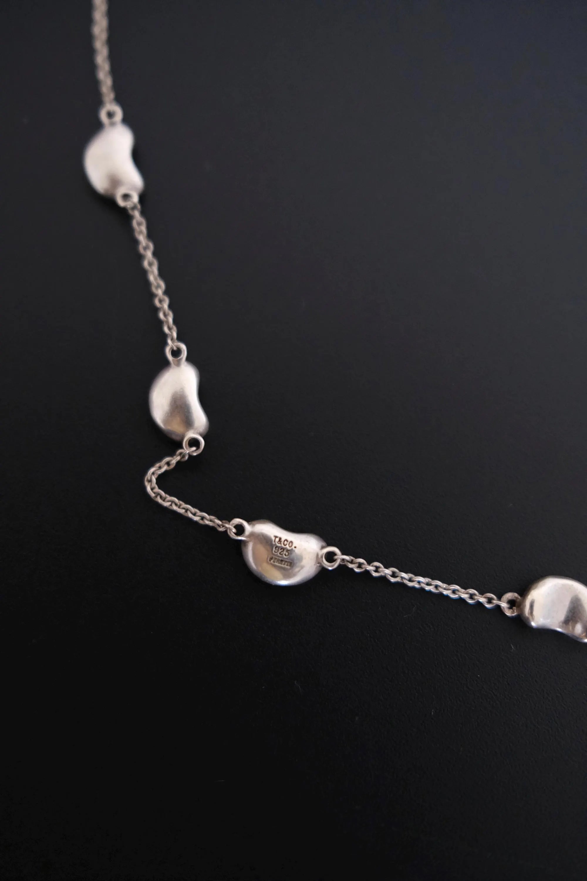 Close-up of TIFFANY & CO signature marking on vintage Elsa Peretti Five Bean silver necklace