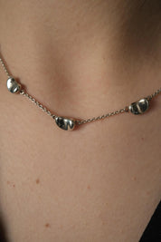 Close-up of Tiffany & Co Elsa Peretti Five Bean silver necklace worn on the neck with five polished organic Bean designs