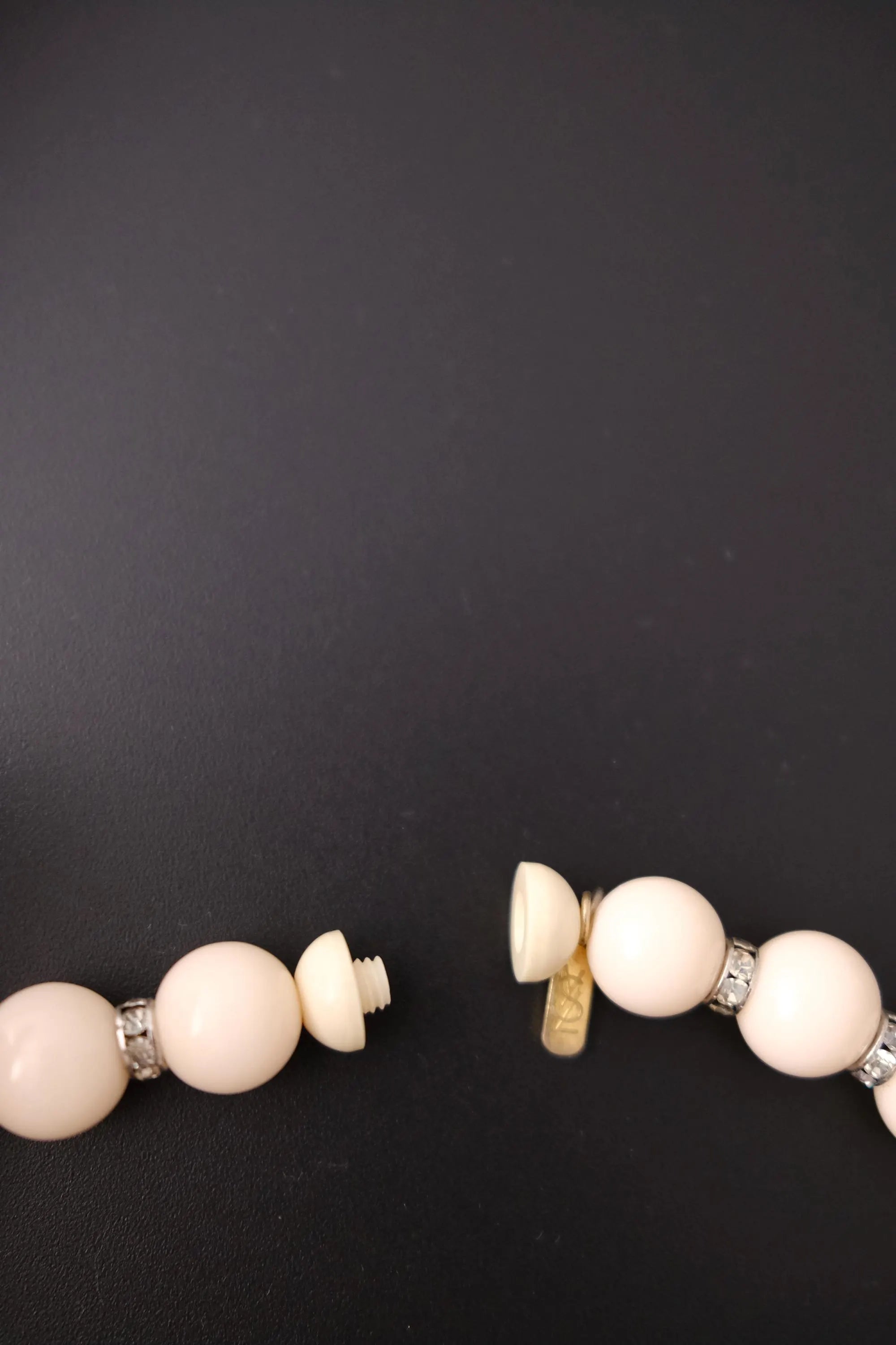 Screw-style closure on vintage Yves Saint Laurent beige beaded necklace with YSL logo charm