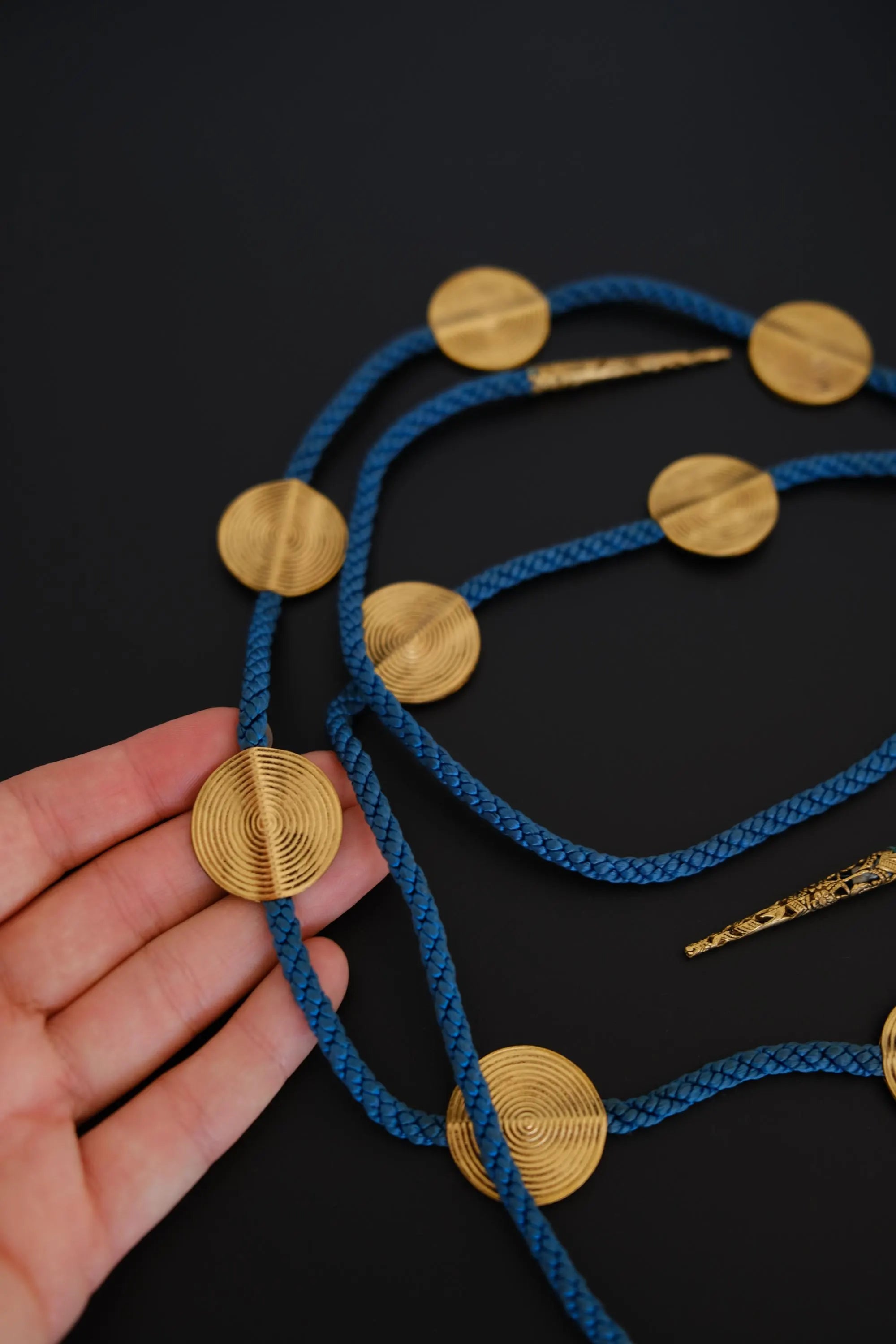 Close-up of large round gold-tone spiral textured medallions on vintage YSL blue cord necklace