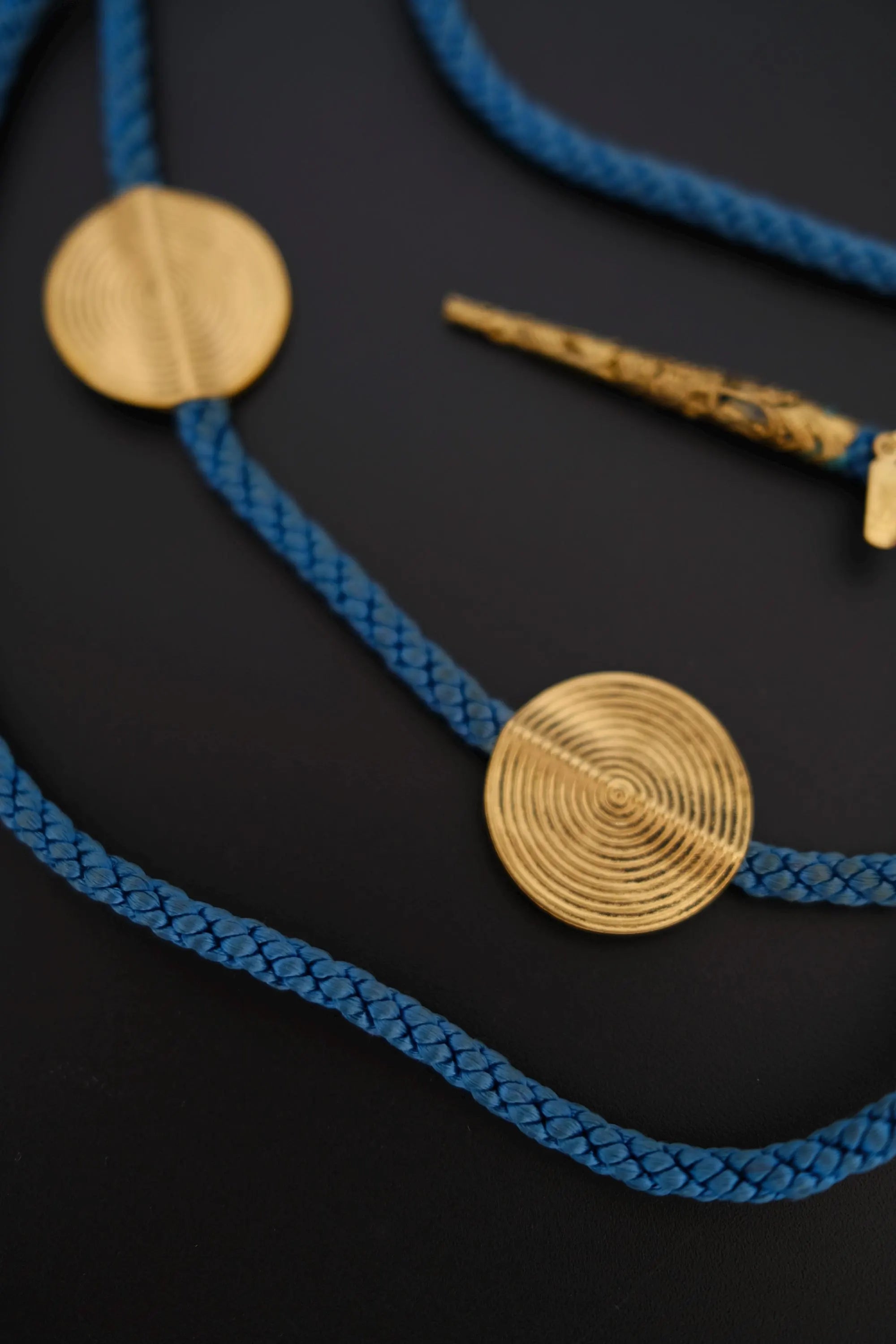 Close-up of large round gold-tone spiral textured medallions on vintage YSL blue cord necklace