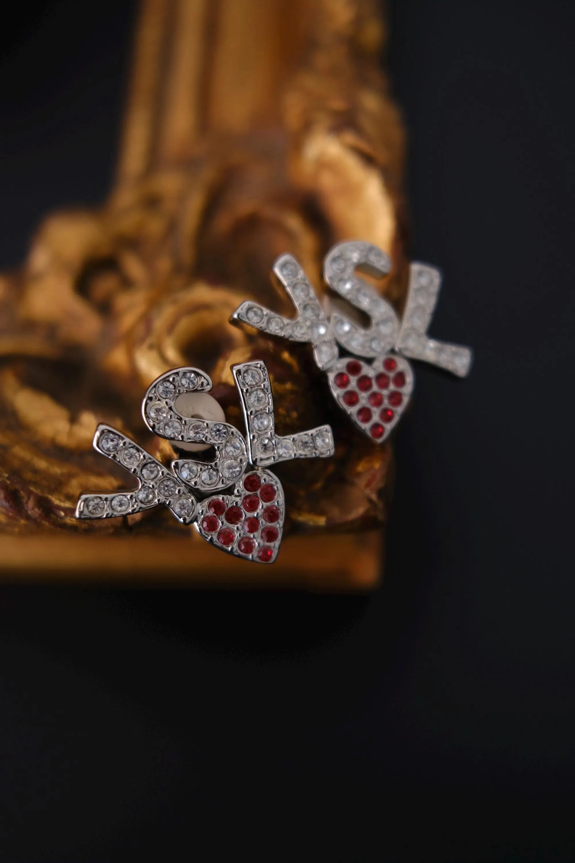 Front view of vintage YSL silver tone earrings with clear crystal logo and red hearts