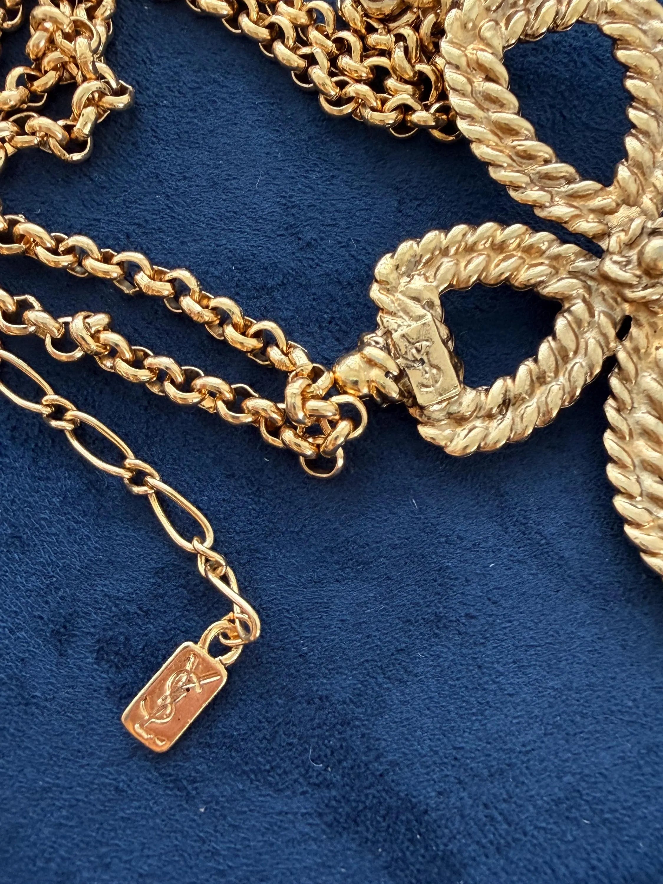 Close-up of YSL openwork cross pendant with textured rope style gold finish